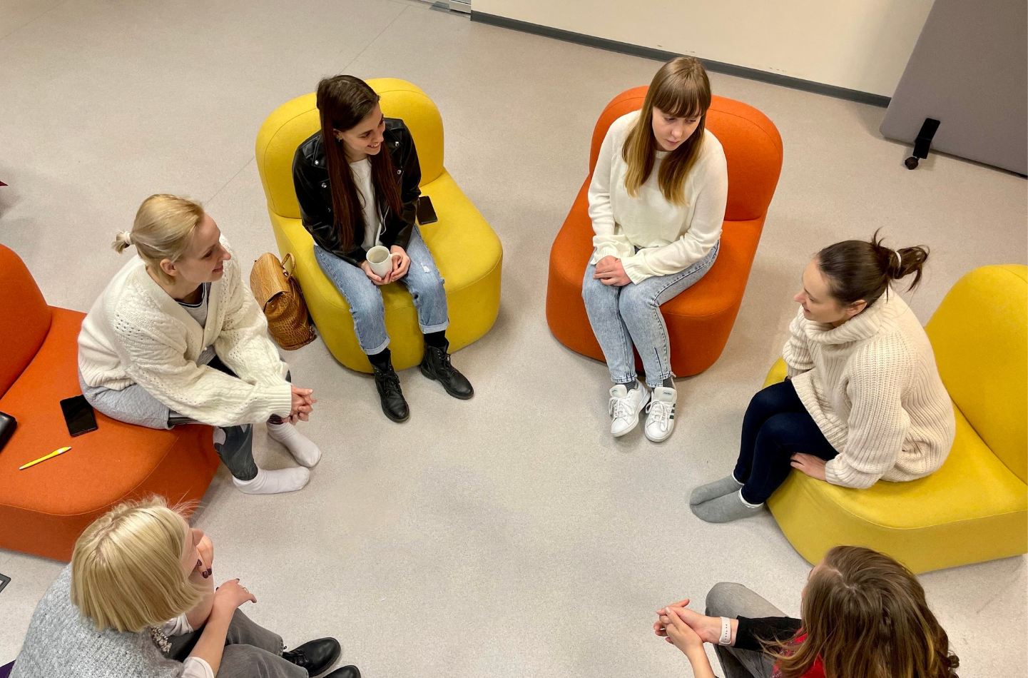 Mokytojos sėdi rate spalvotuose krėsluose ir dalijasi patirtimi